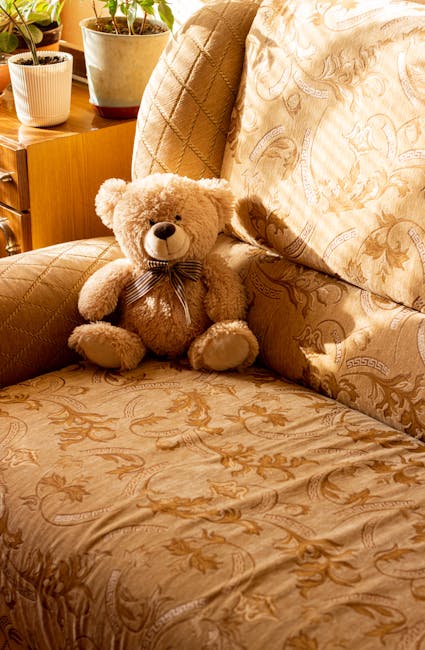 An opulent, luxurious room featuring ornate, gold-accented moldings and detailed wall paneling, illuminated by a large, intricate crystal chandelier hanging from a decorated ceiling. There are tall, elegant windows with heavy, dark blue drapes and valances, allowing natural light to filter into the space. The polished wooden floor displays a herringbone pattern and reflects the ambient light, enhancing the room's grandeur. Opposite the windows, a central decorative water fountain is situated on the floor, surrounded by a small circular platform. Along the walls, antique-style chairs with gold frames and upholstered seats are neatly arranged, some positioned near the windows. The room appears highly clean and well-maintained, exemplifying careful surface cleaning and decorative item dusting, consistent with the services provided by crystalpalacecarpetcleaning.co.uk for upholstery cleaning and deep cleaning of luxurious spaces.